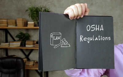 Hand holding notebook with a law book/gavel, says OSHA Regulations in handwriting